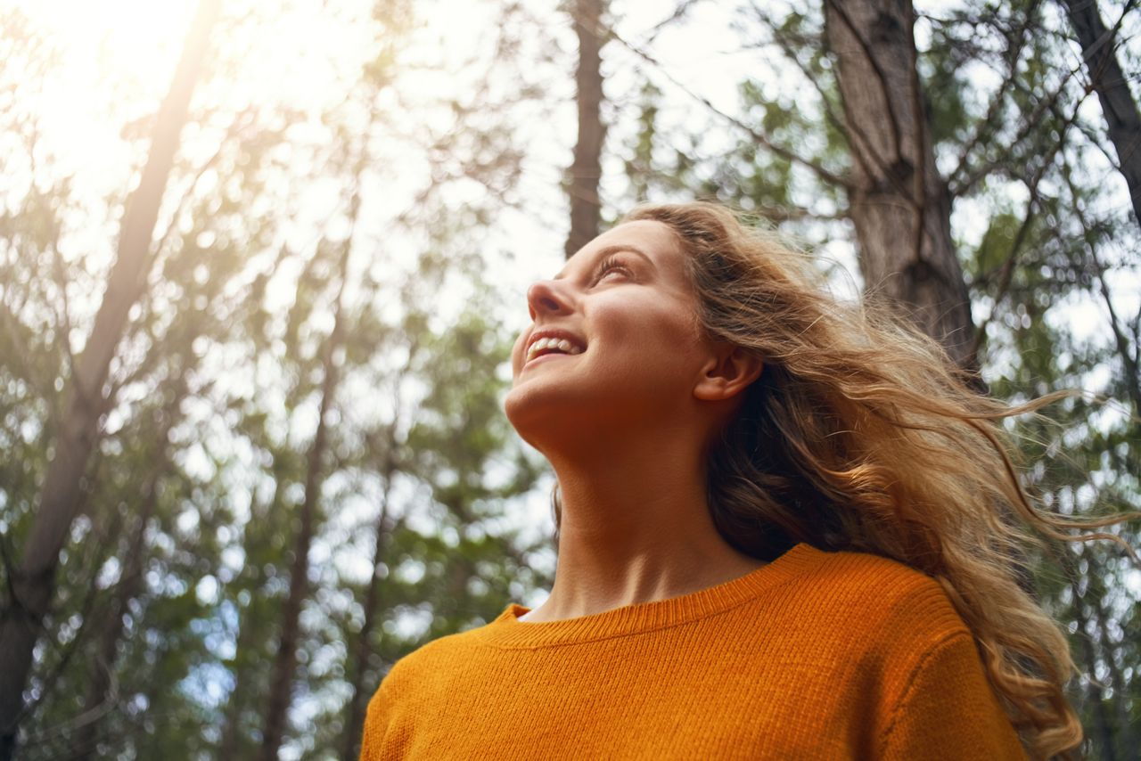 Una giovane donna sorridente si gode il tempo trascorso sotto il sole in una foresta